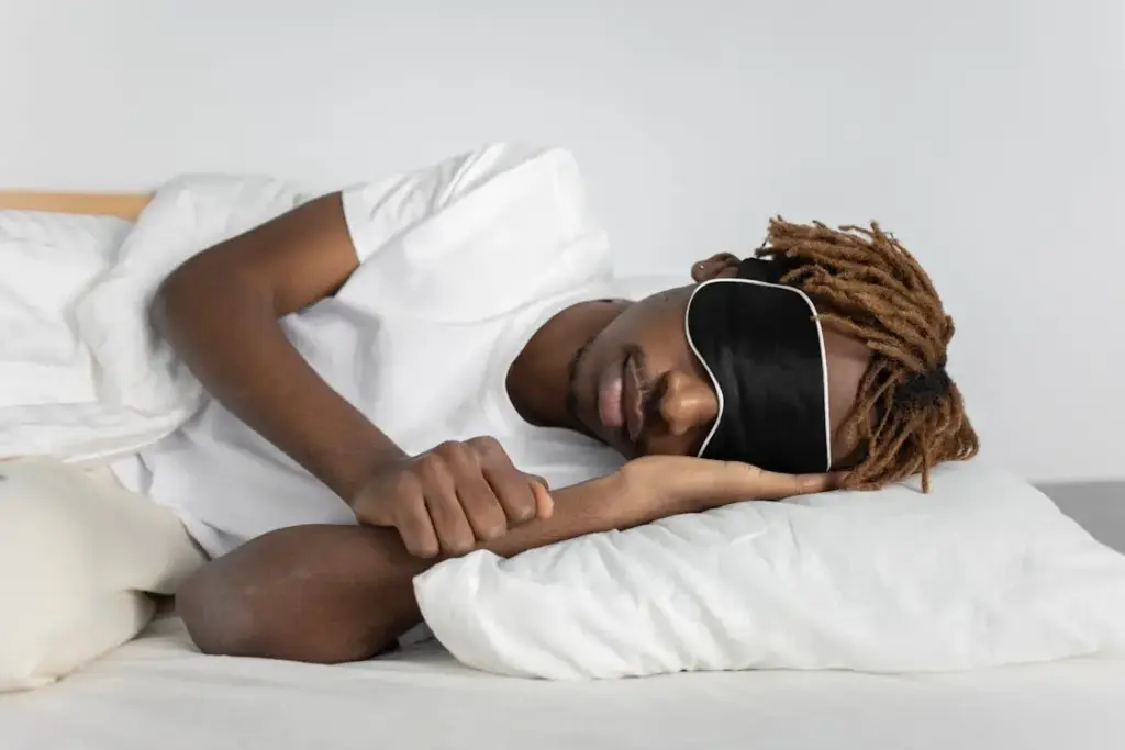Person wearing sleep mask lying on white pillow in bright bedroom setting