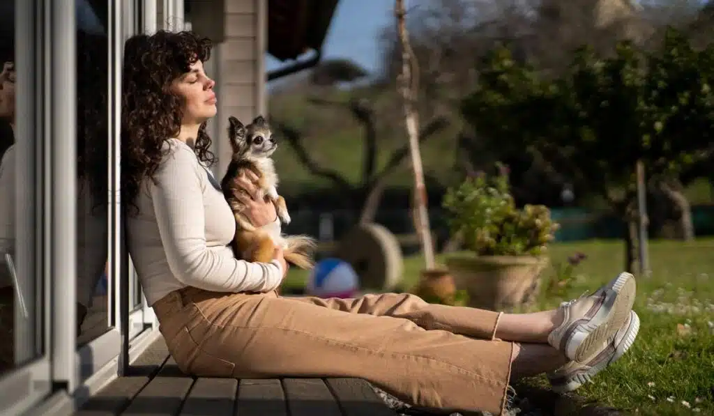 Woman sitting on patio deck holding a small chihuahua dog