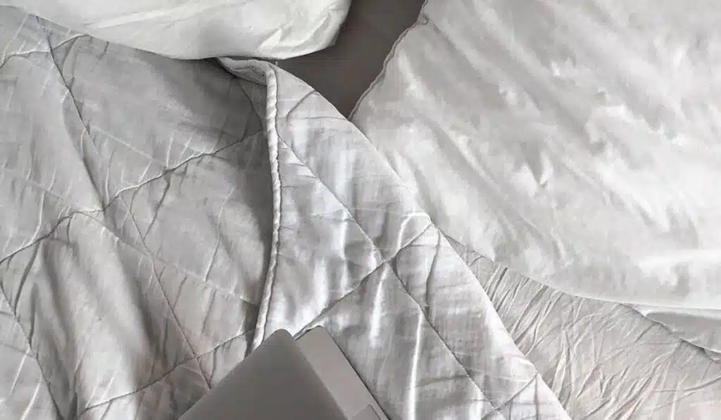 Laptop on white quilted bedding for a cozy workspace