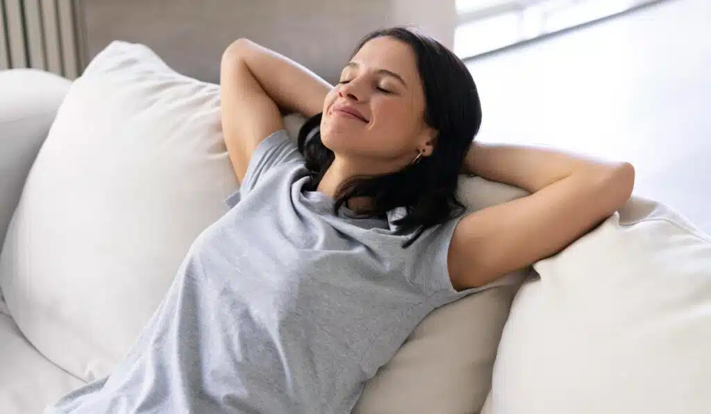 Woman relaxing with hands behind head on white sofa