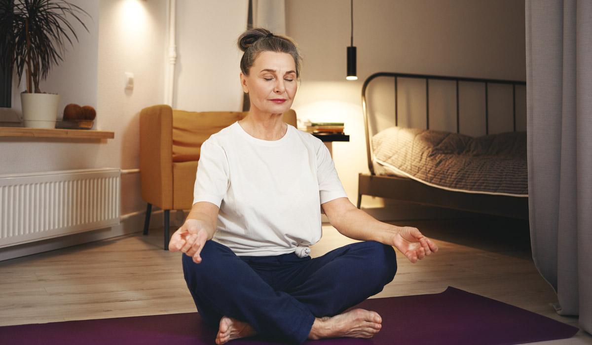 Senior woman meditating on a yoga mat at home