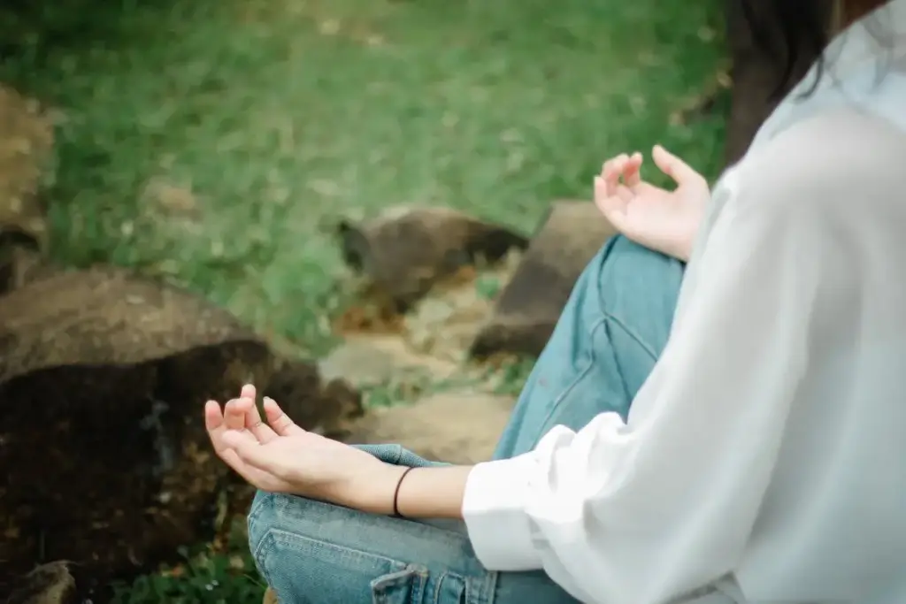 Person in white shirt meditating outdoors on grass with rocks nearby