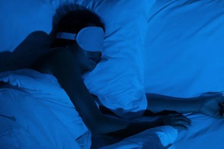 Person sleeping with eye mask in bed under blue lighting