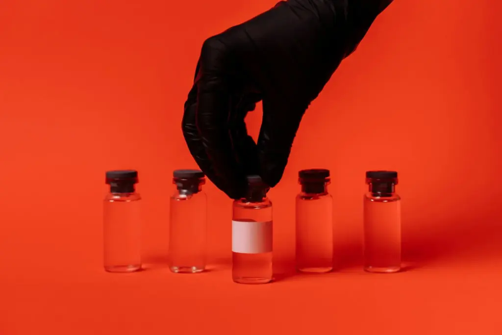 Black-gloved hand picking up a glass vial on bright orange background