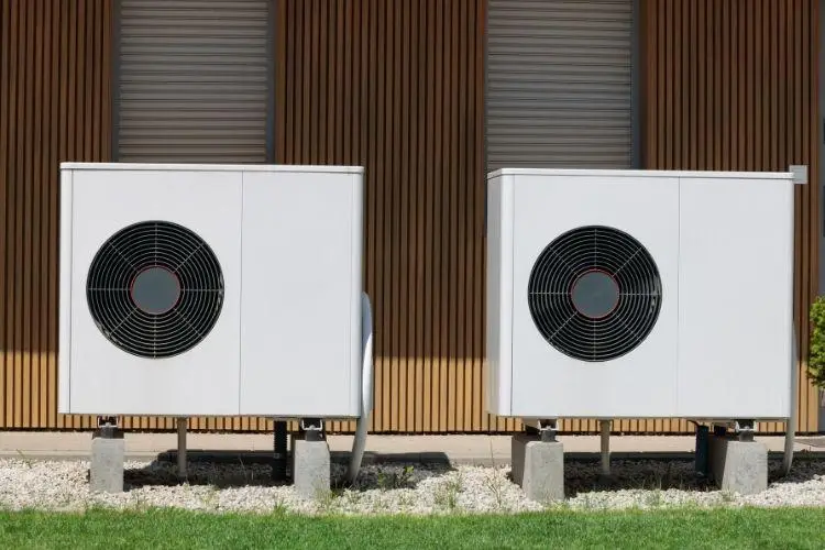 Two outdoor air conditioning units on concrete slabs against wooden slat wall