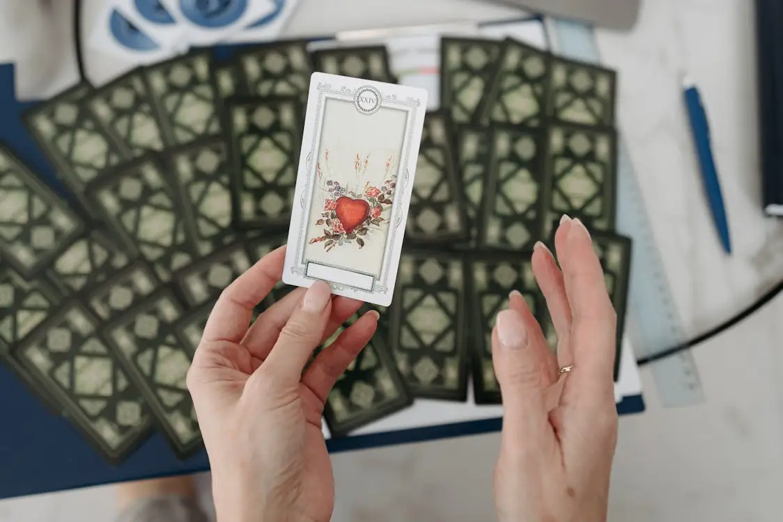 Hands holding tarot card with heart design over spread cards on table
