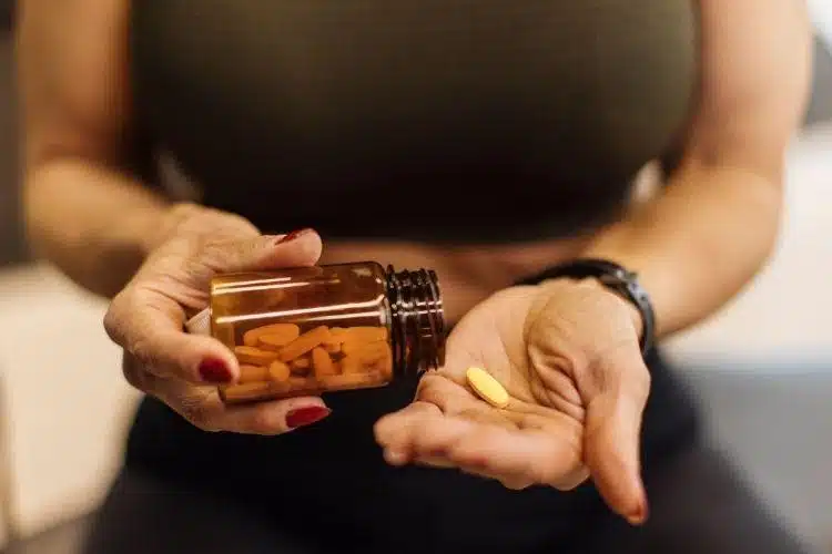 Woman with pill bottle and supplement pill in hand