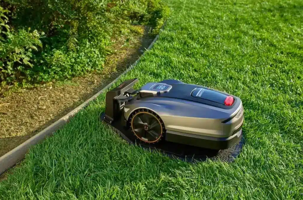 Robotic lawn mower on green grass near garden bed in outdoor setting