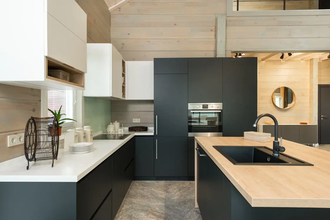 Modern kitchen with sleek black cabinetry, integrated oven, wooden countertops, and light wood walls