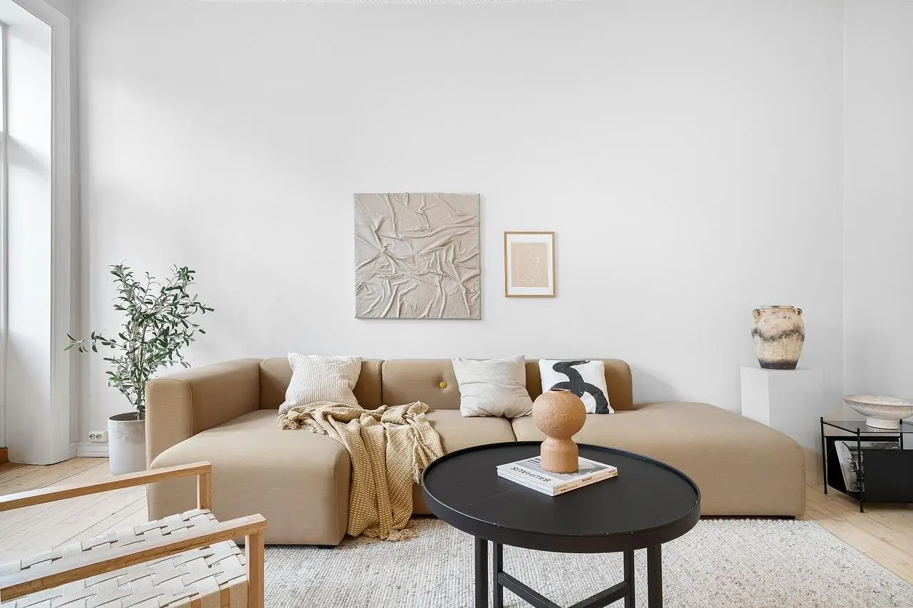 Modern living room with beige sectional sofa, neutral artwork, and round coffee table with decor