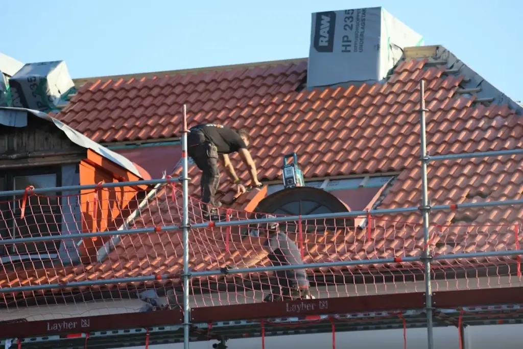 Construction workers installing roof tiles on scaffolding under clear sky