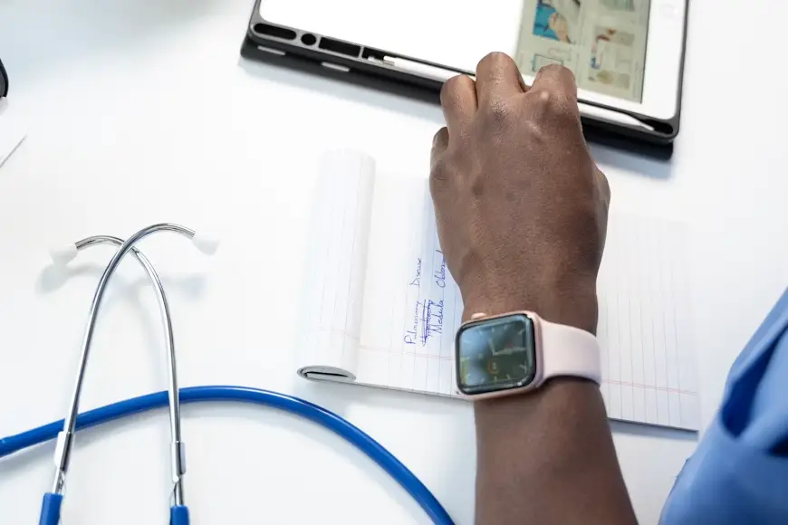 Doctor writing notes on notepad beside stethoscope and tablet in bright office setting