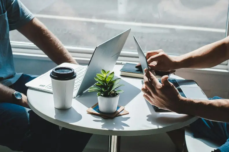 Two people at round table with laptops and tablet in bright office setting