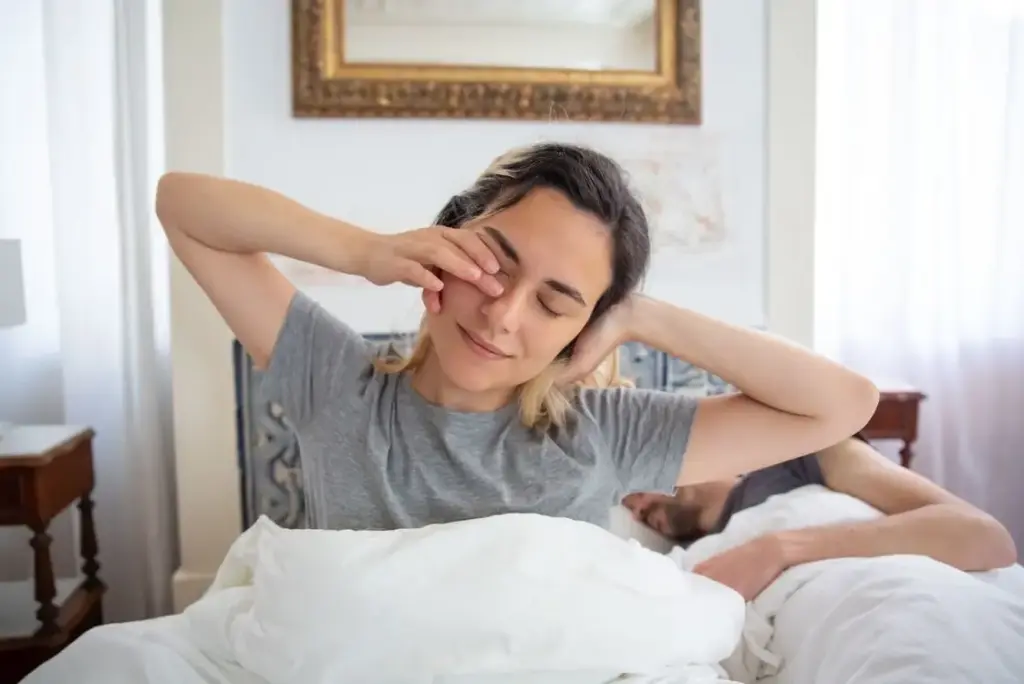 Woman waking up in bed, stretching arms, bright bedroom with soft lighting