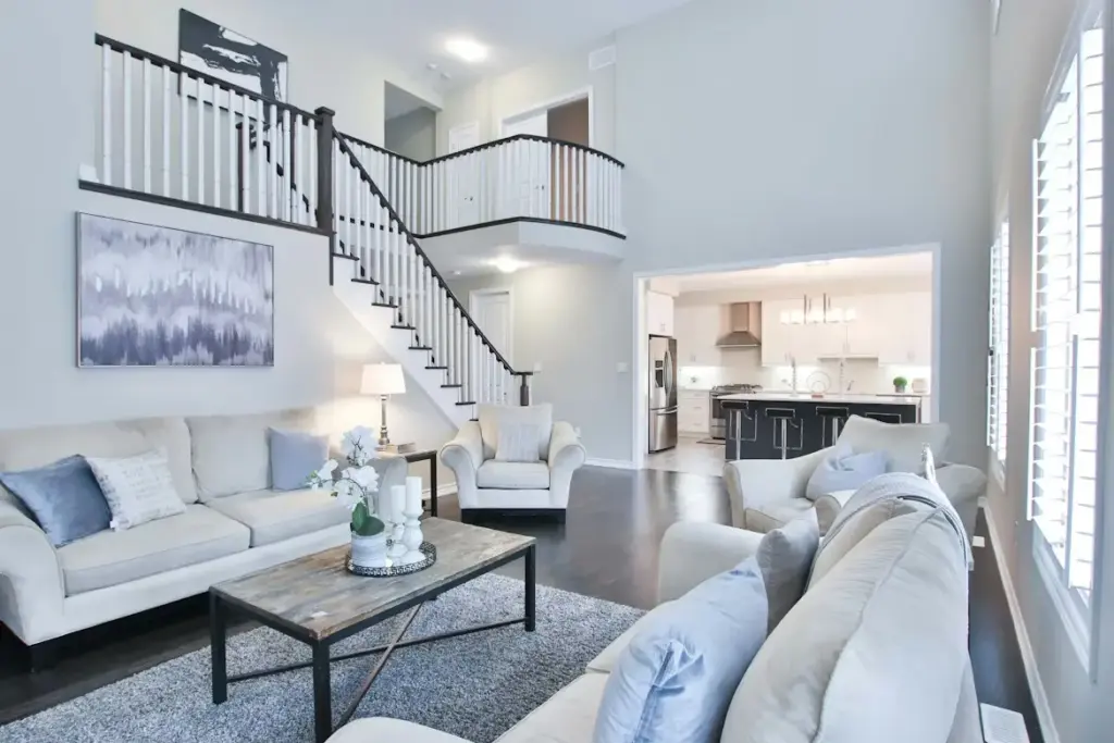 Spacious living room with neutral sofas, modern artwork, and view into bright kitchen area
