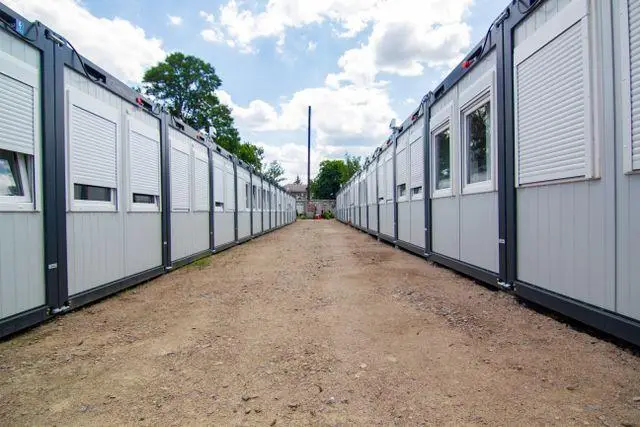 Two rows of temporary housing units facing each other on a gravel path under cloudy sky