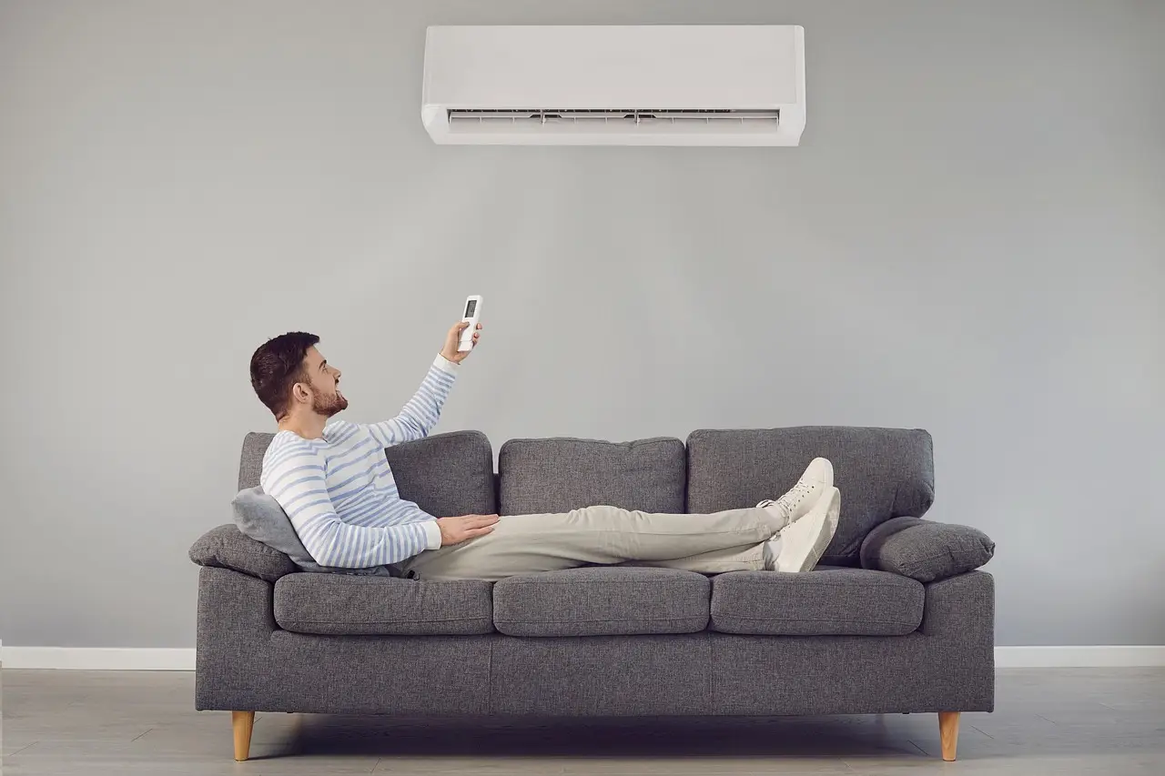 Man lying on gray sofa using remote to control air conditioner in modern living room