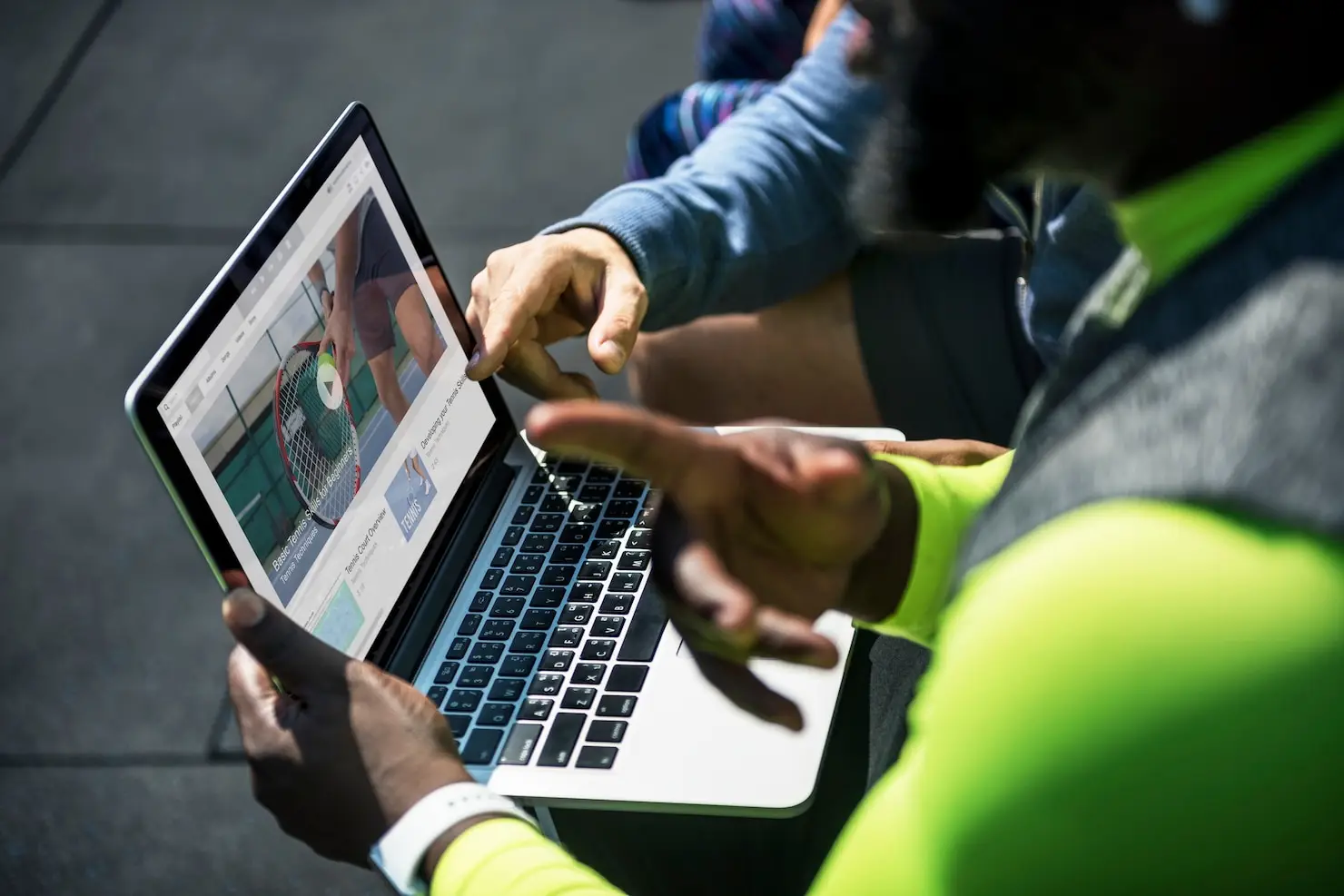 Person watching tennis video on laptop screen outdoors in bright daylight