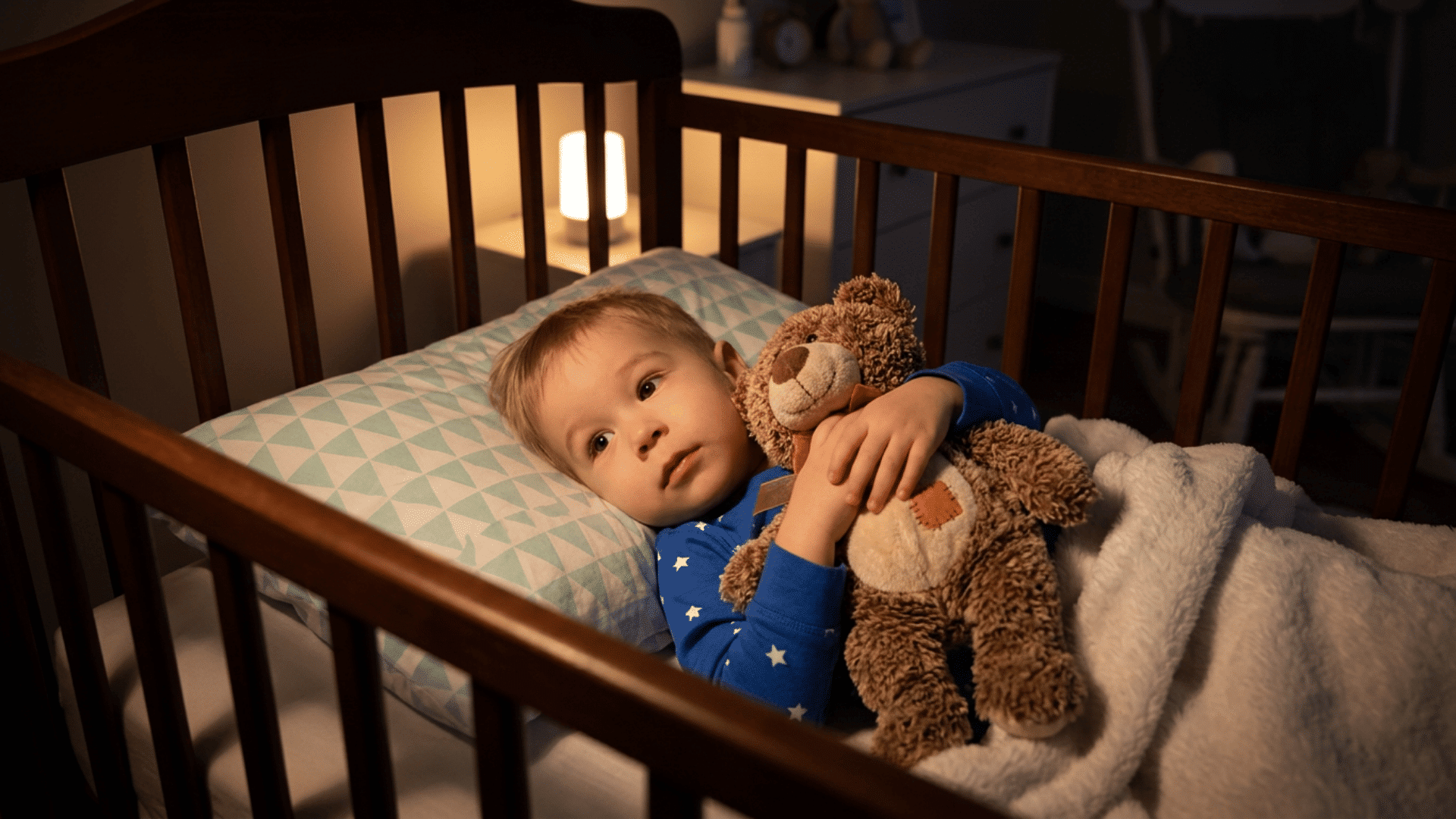 awake toddler holding a stuffed toy in a crib during a sleep regression.