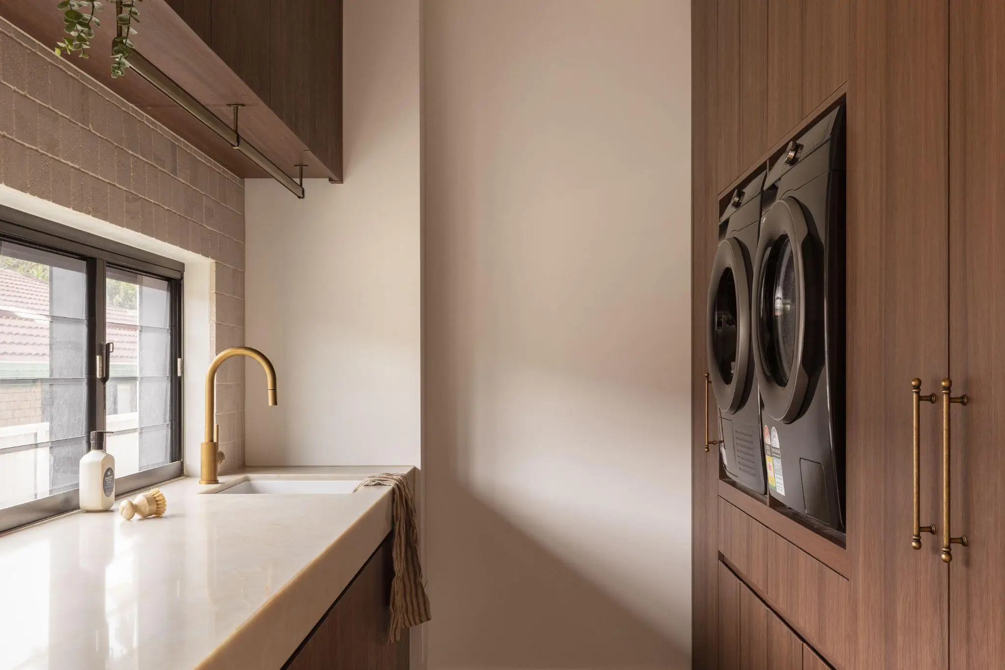 Stacked black washer and dryer in modern laundry room with wood cabinets and brass faucet