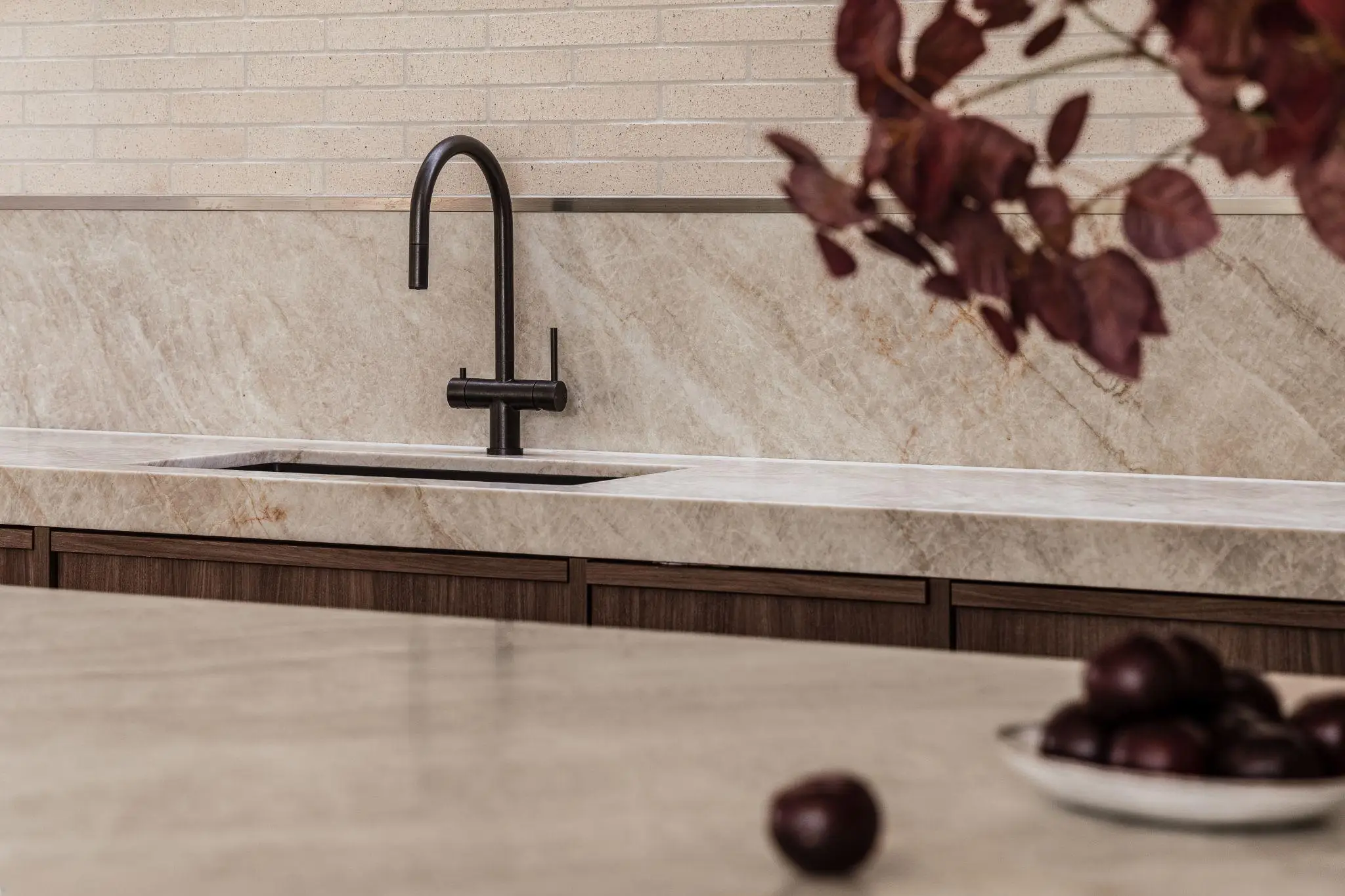 Black faucet and marble countertop in modern kitchen with wooden cabinetry and decorative branches