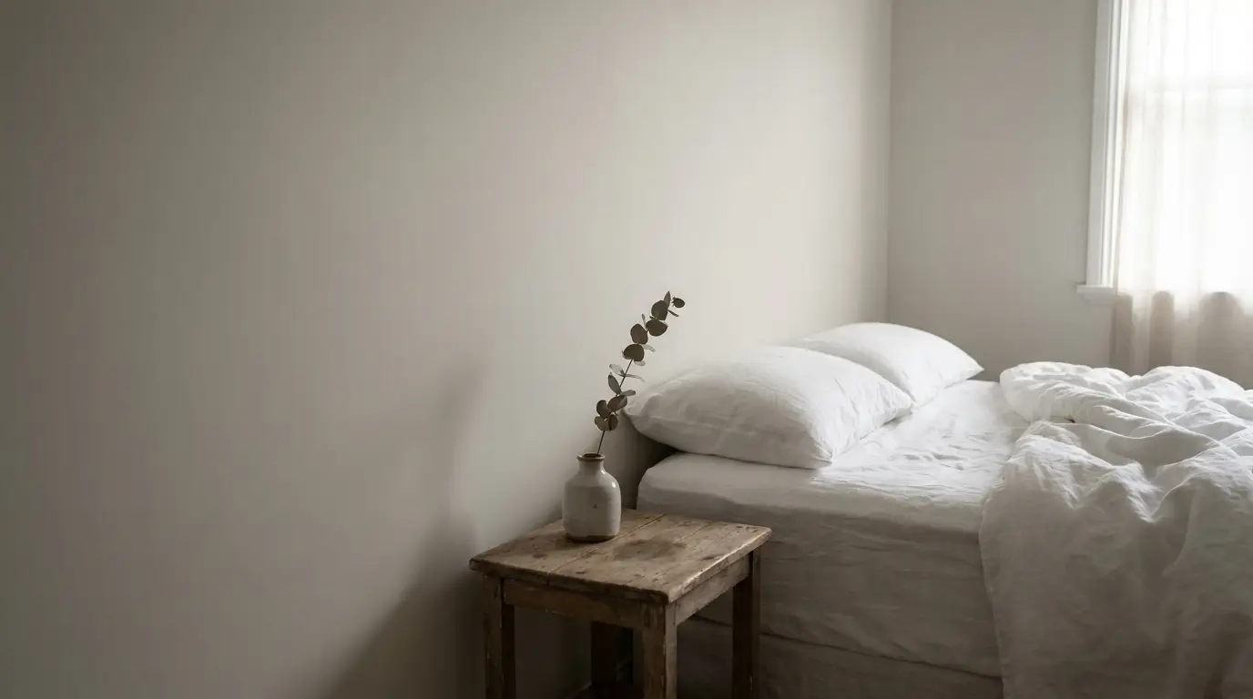 Minimalist bedroom with white bedding, wooden side table, and ceramic vase with branch