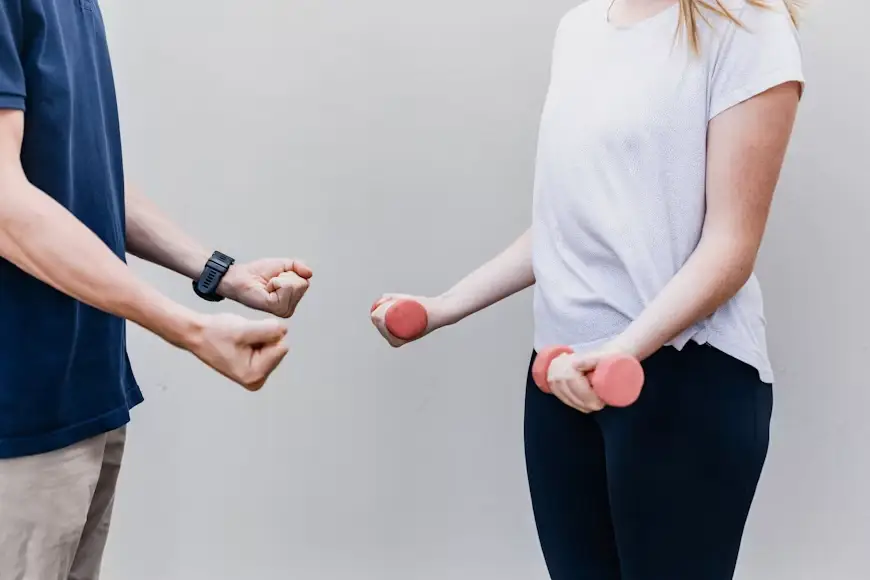 Two people exercising with pink dumbbells in an outdoor setting