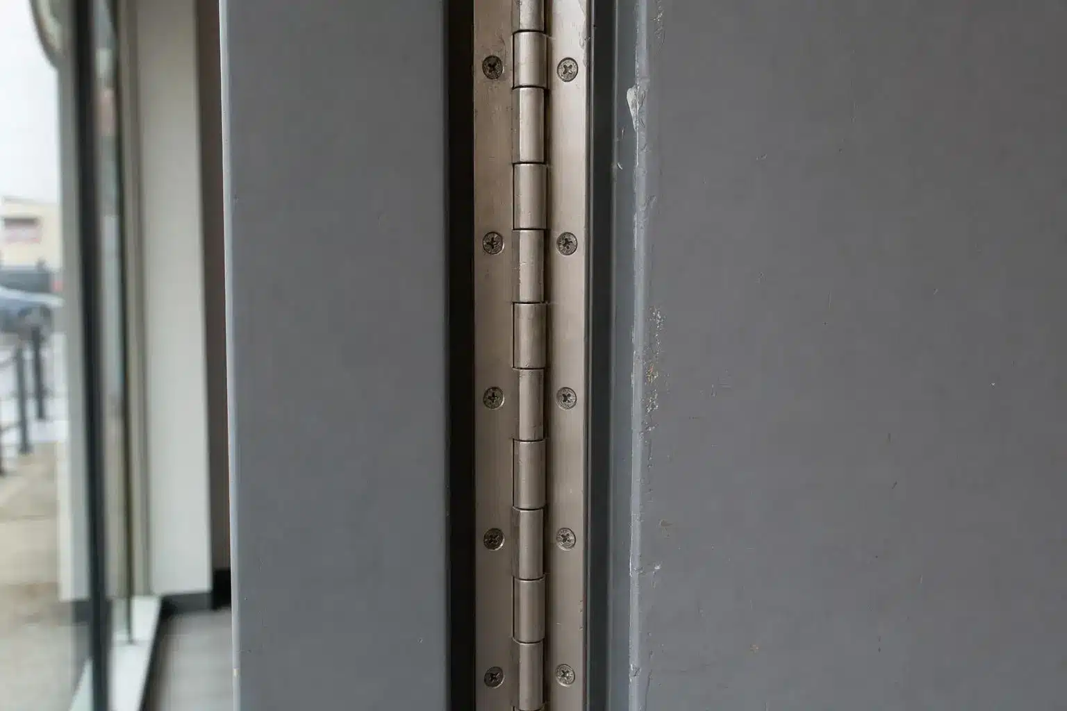 Stainless steel door hinge on a gray metal door in a modern interior setting