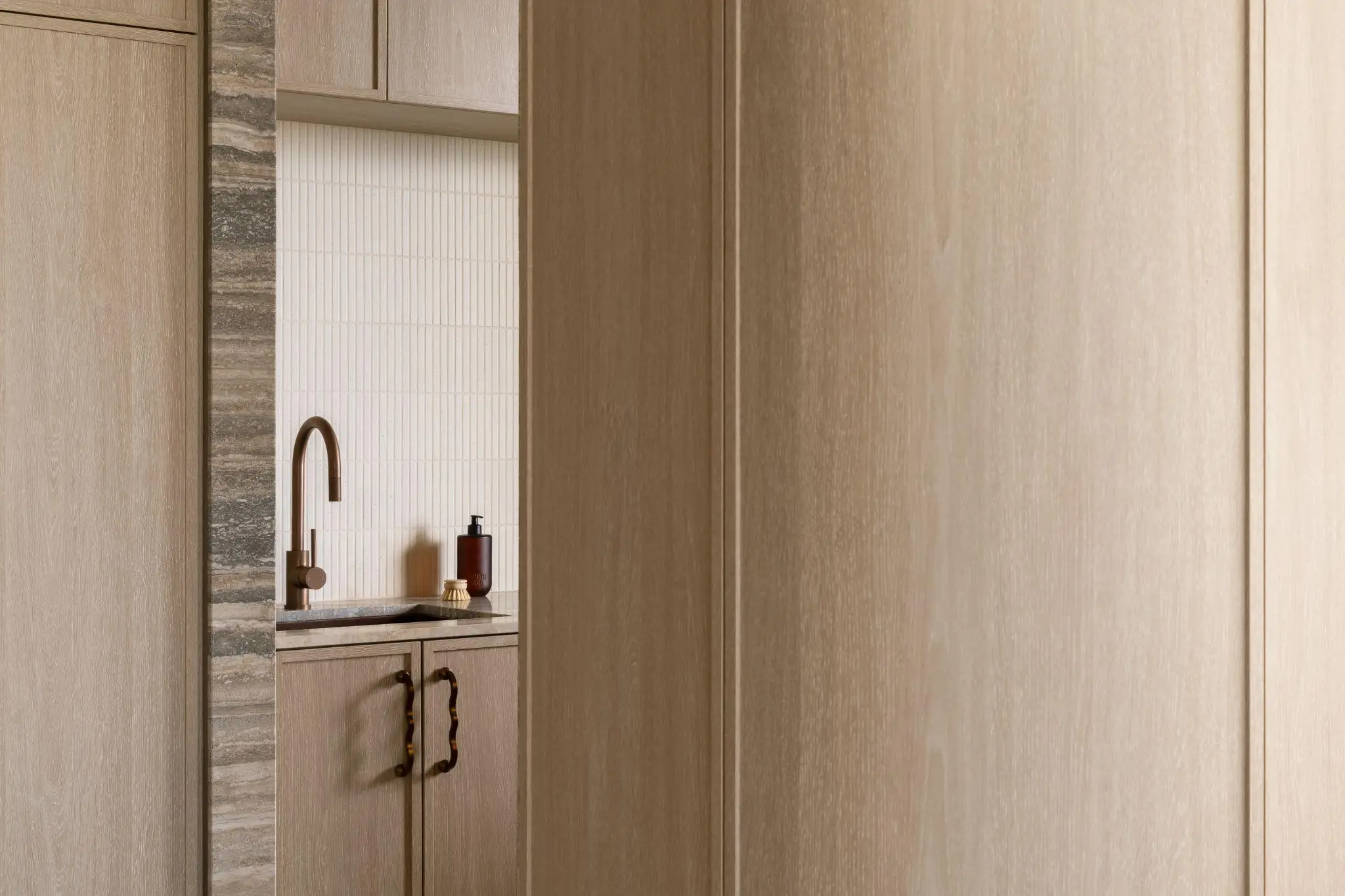 Wood-paneled kitchen with brass faucet and light backsplash tiles