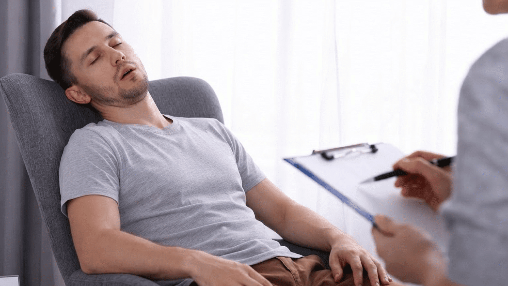 Sleep specialist observes a drowsy man resting in a chair during an idiopathic hypersomnia checkup.
