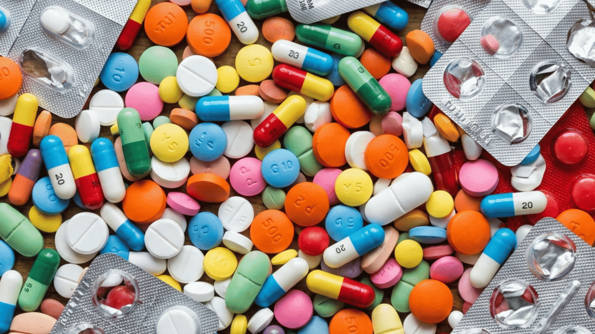 Assorted colorful pills and medicine tablets arranged with blister packs on a wooden surface.