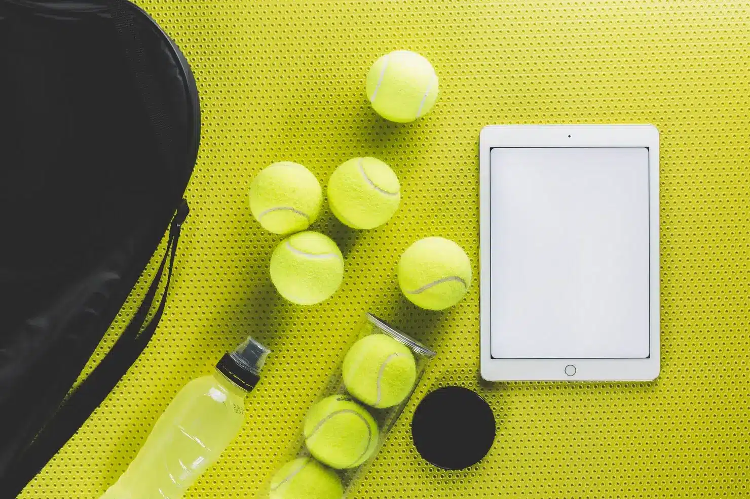 Tennis balls, tablet, and water bottle on yellow perforated surface