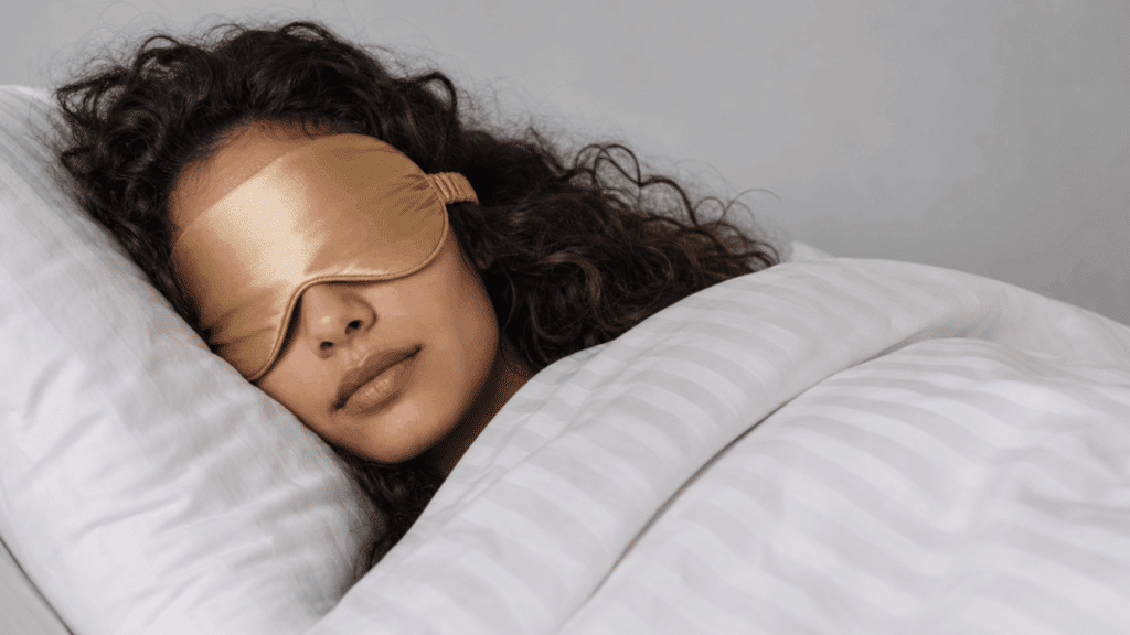 Person sleeping peacefully in bed wearing a sleep mask under a white blanket.