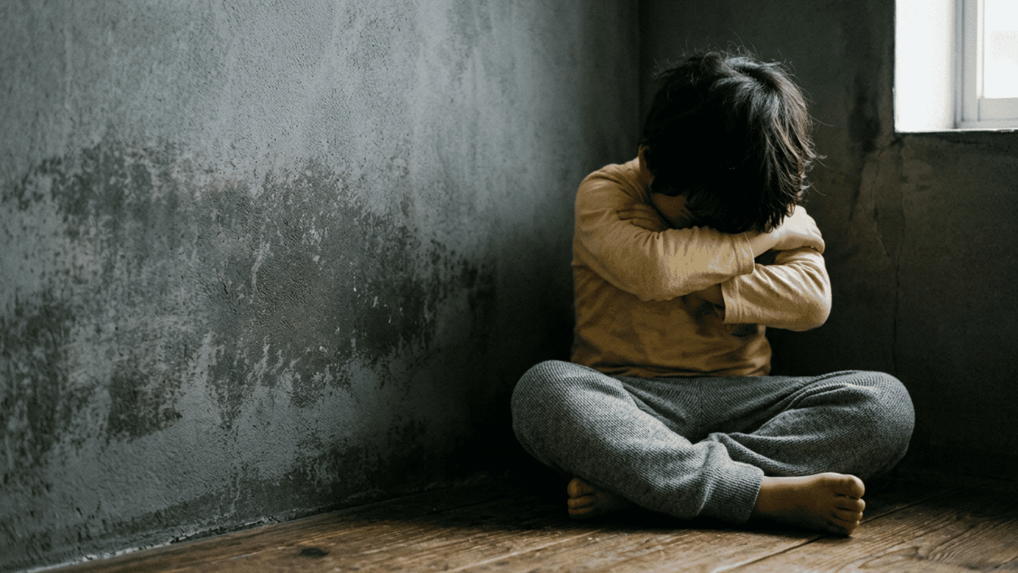 Person sitting alone in a dim room with head down, showing feelings of distress or sadness.