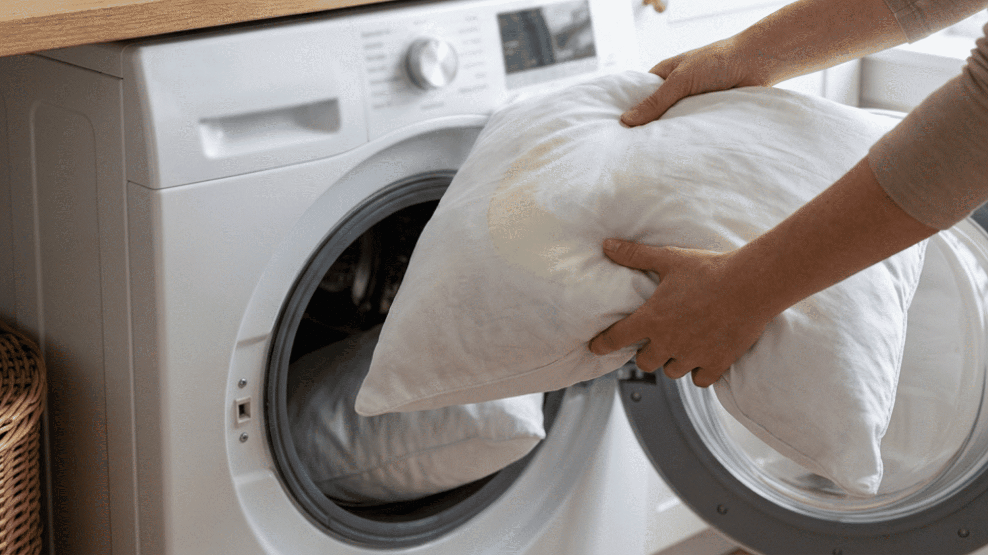 person places two stained white pillows inside an open front-loading washing machine next