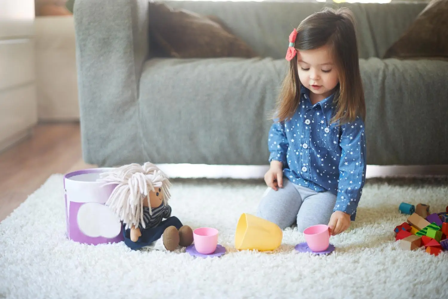 Young girl having pretend tea party with dolls on a fluffy rug indoors