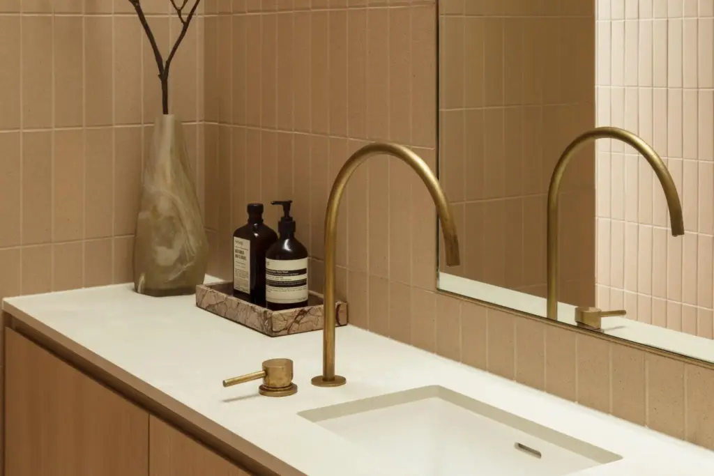 Modern bathroom vanity with brass faucet on beige countertop and decorative vase with branches