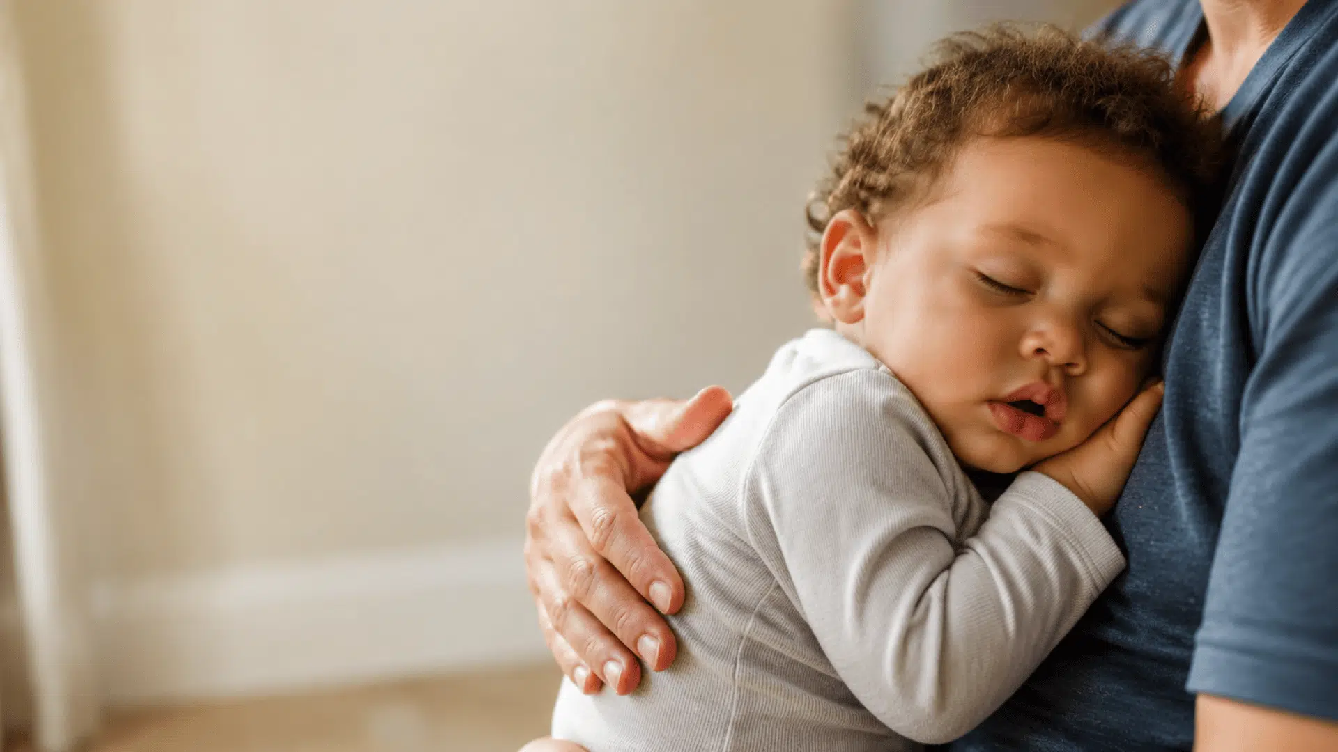 sleeping 13-month-old toddler resting safely in a parent’s arms