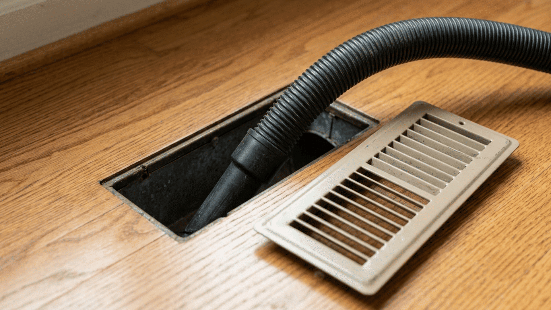vacuum hose inserted into an open floor duct with the vent cover removed