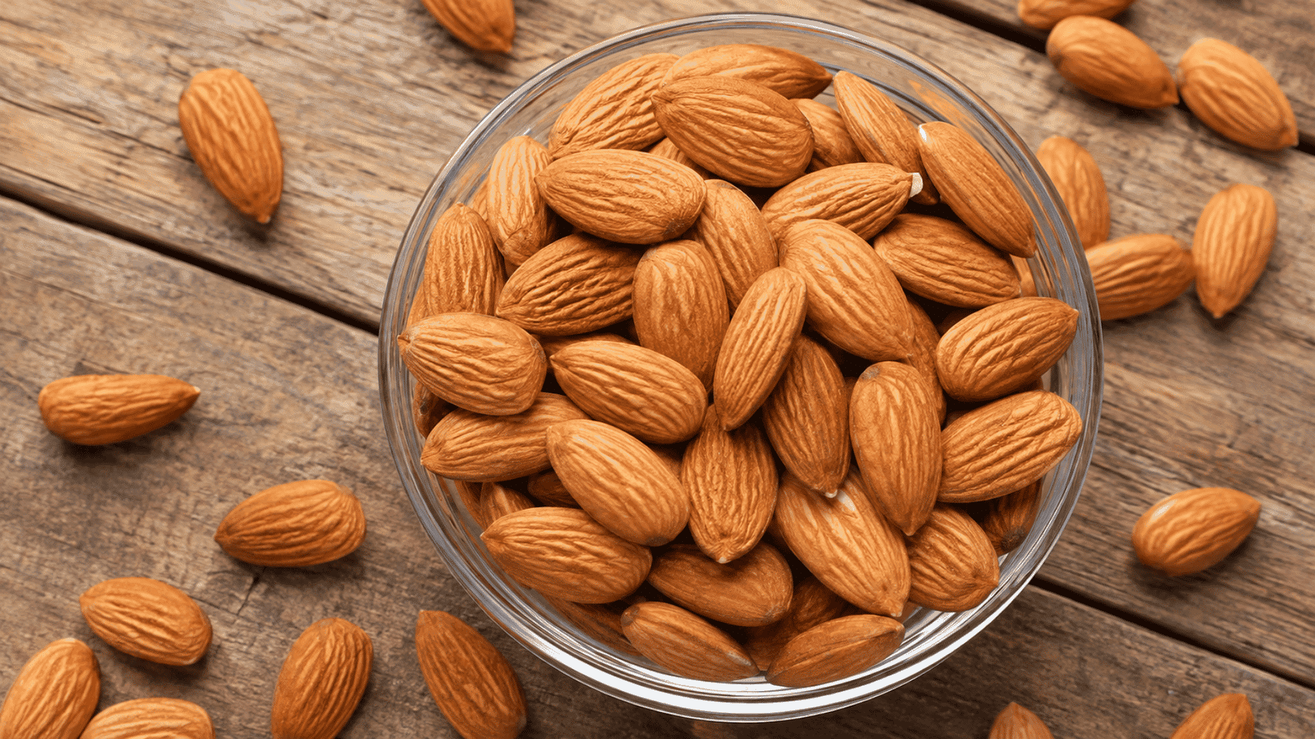 almonds in a clear glass bowl scattered across a rustic wooden table
