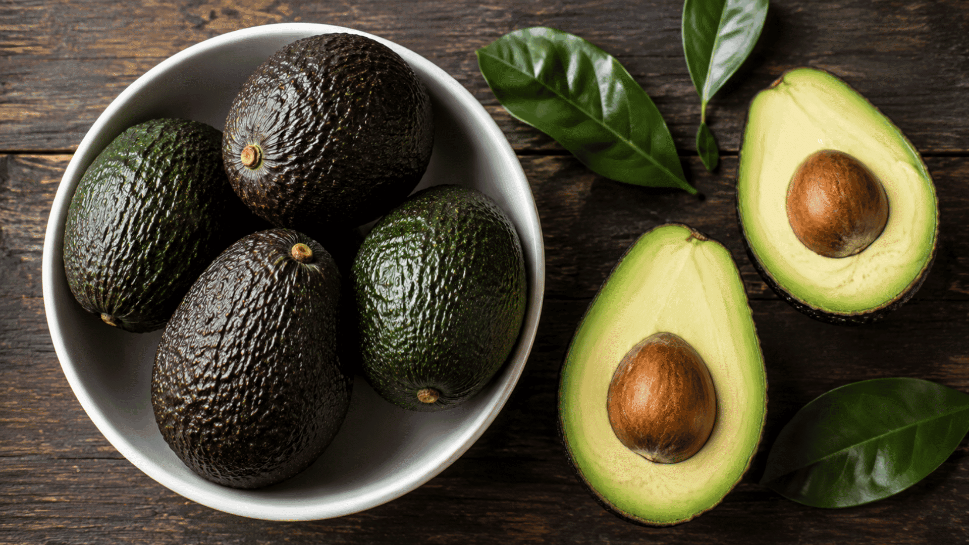 whole and halved avocados with green leaves on a dark wooden table