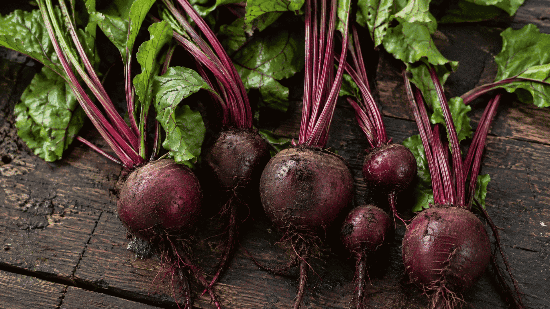 fresh beetroots with leafy stems arranged on a rustic wooden surface