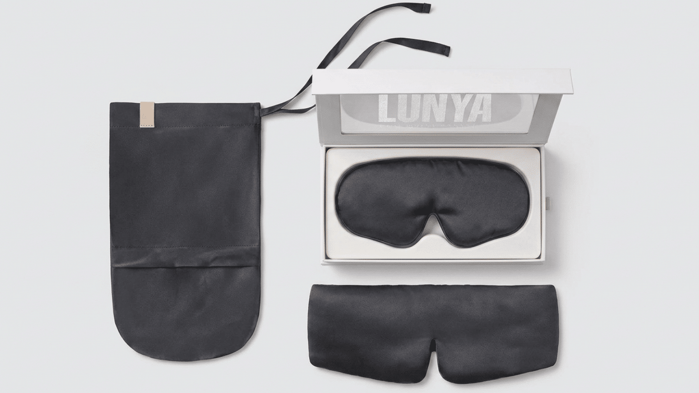 black Lunya washable silk sleep mask displayed with its box, travel pouch, and folded cover laid out