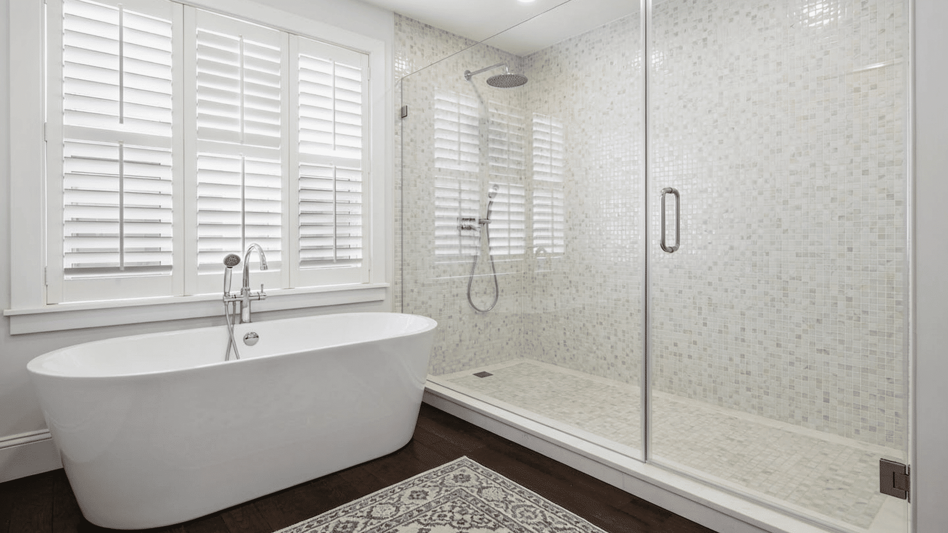 bright curbless walk-in shower with mosaic tiles, glass panels, and freestanding tub