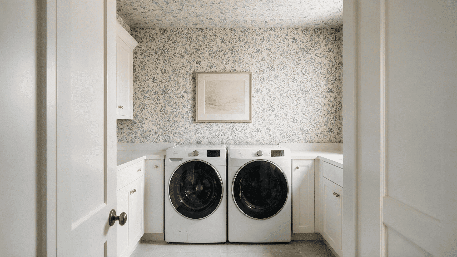 bright laundry room with floral wallpaper, white cabinets, and two front-loading machines