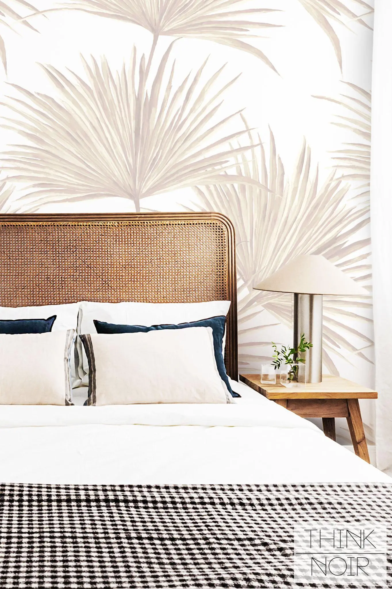 Woven rattan headboard with patterned bedding against palm leaf wallpaper in a bright bedroom