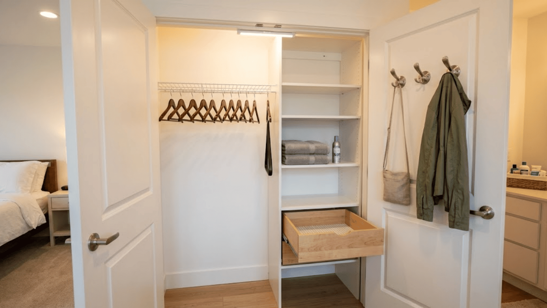 Open guest closet with empty wooden hangers, open drawer, and jacket on a door hook.