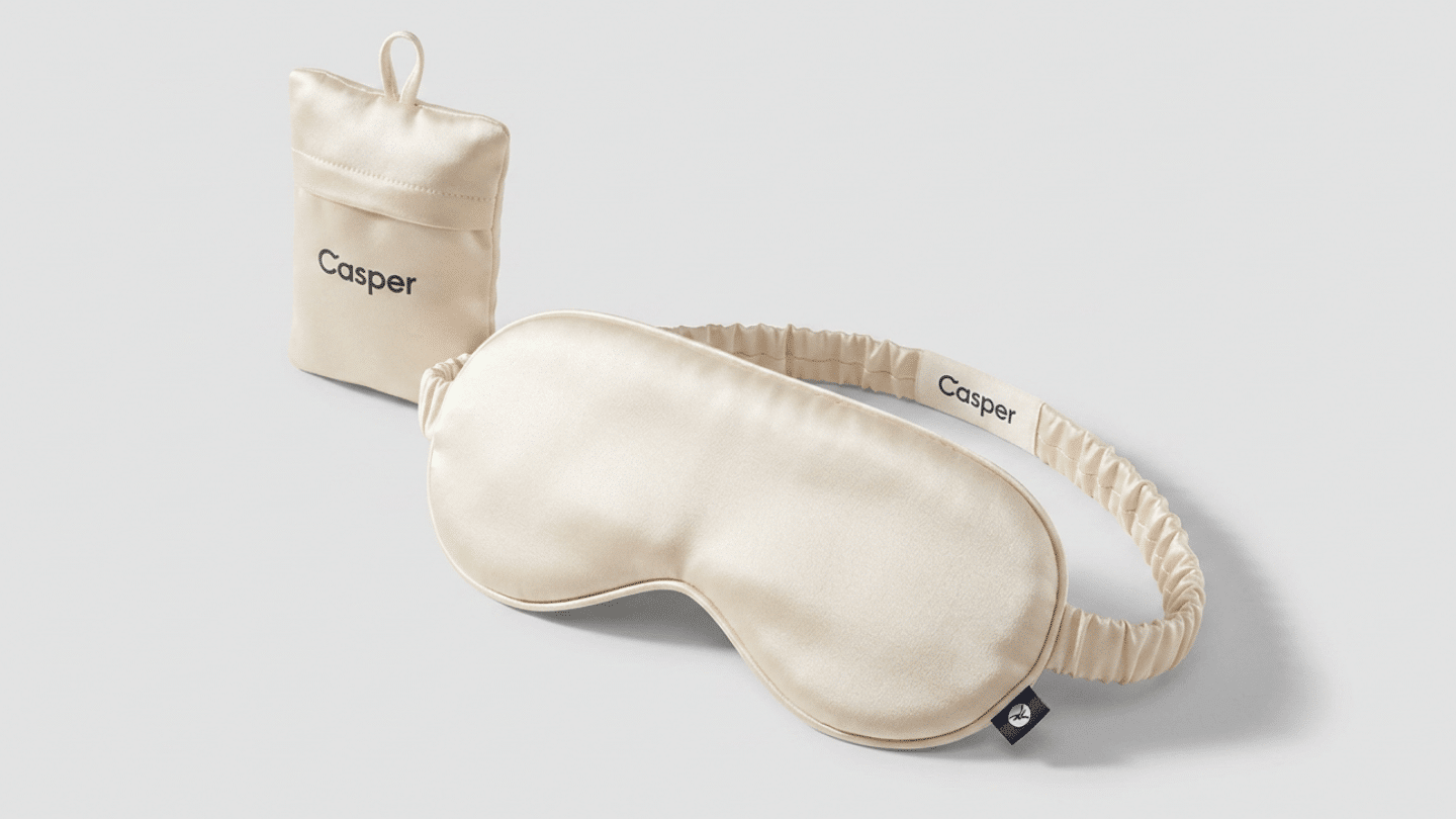 cream Casper silk sleep mask with covered elastic band and matching pouch on white surface laid flat