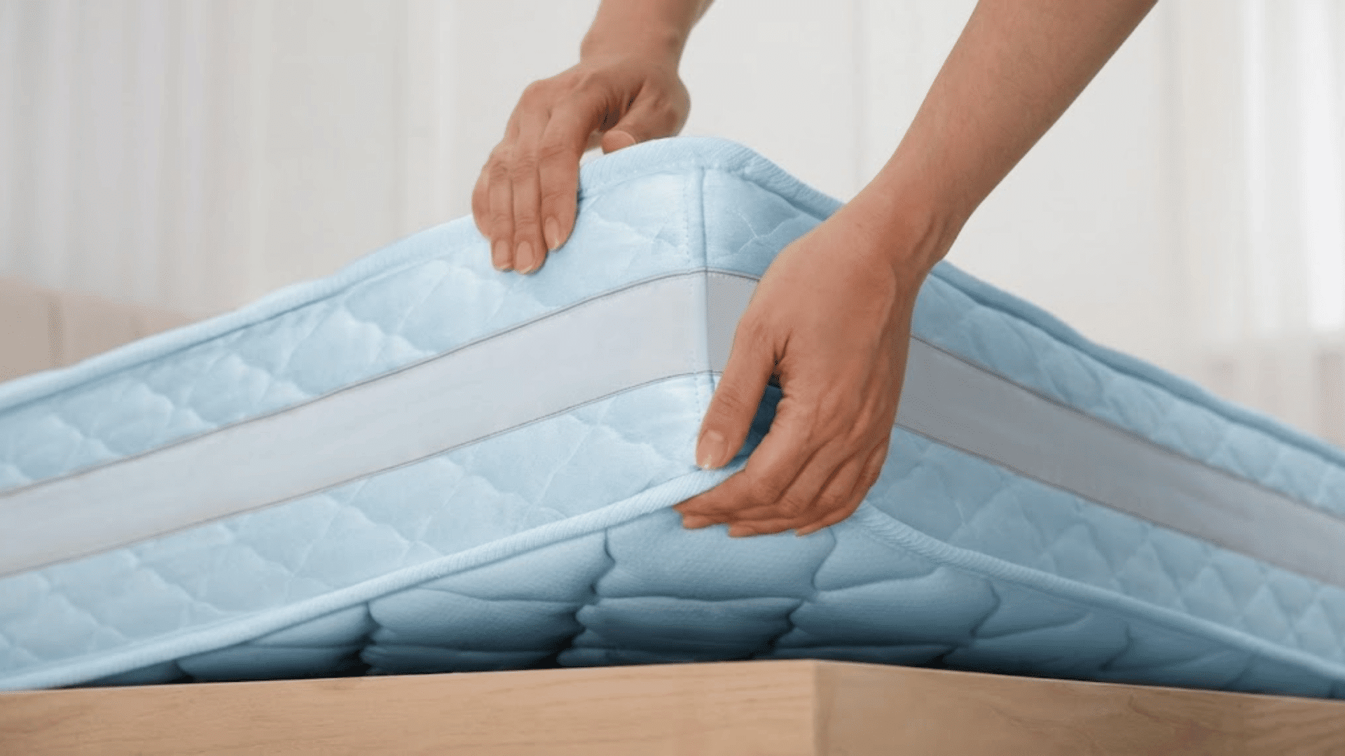 hands lifting a mattress cover to show internal foam layers and protective fabric material