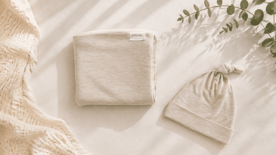 folded beige solly baby swaddle and matching knotted hat on a cream background